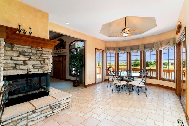 dining space with french doors, ceiling fan, light tile floors, a fireplace, and a tray ceiling