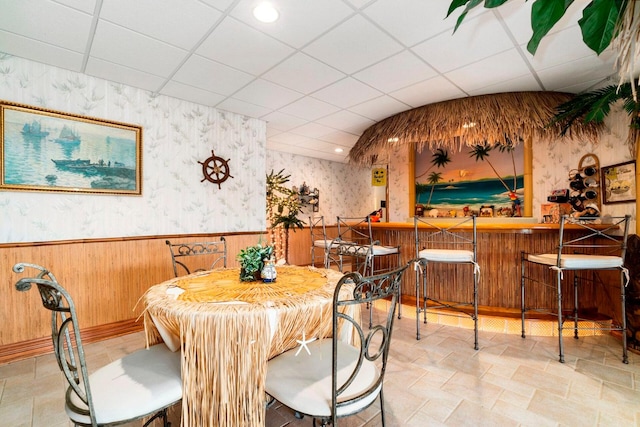 dining space featuring a paneled ceiling, indoor bar, and light tile flooring