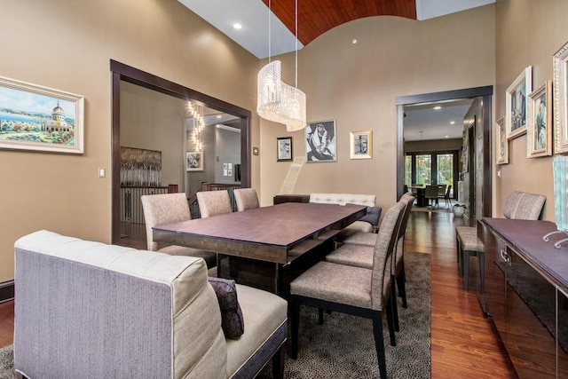 dining space with a notable chandelier, a towering ceiling, and dark hardwood / wood-style flooring