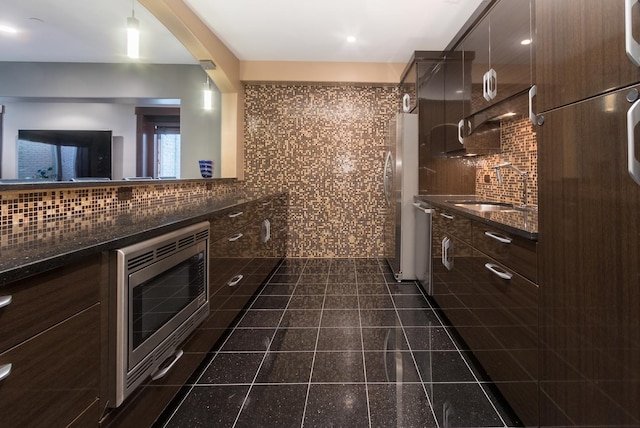 kitchen featuring sink, dark tile flooring, hanging light fixtures, appliances with stainless steel finishes, and backsplash