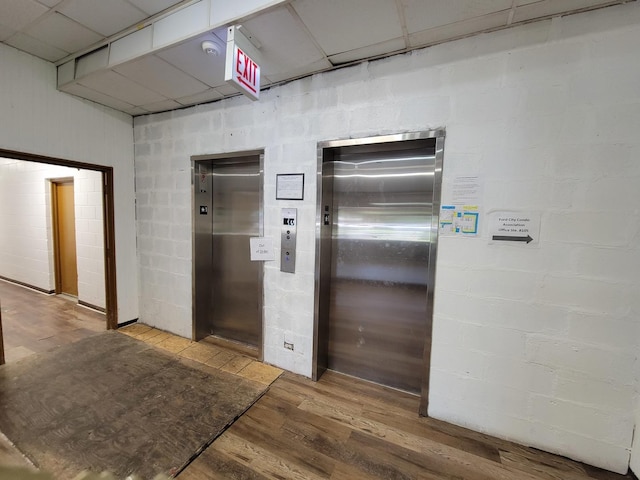 corridor with a paneled ceiling, wood-type flooring, and elevator