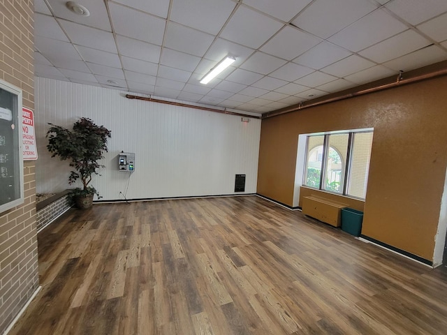 spare room with dark wood-type flooring, brick wall, and a drop ceiling