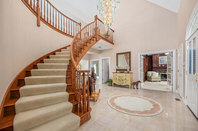 staircase with an inviting chandelier, a healthy amount of sunlight, light tile floors, and a towering ceiling