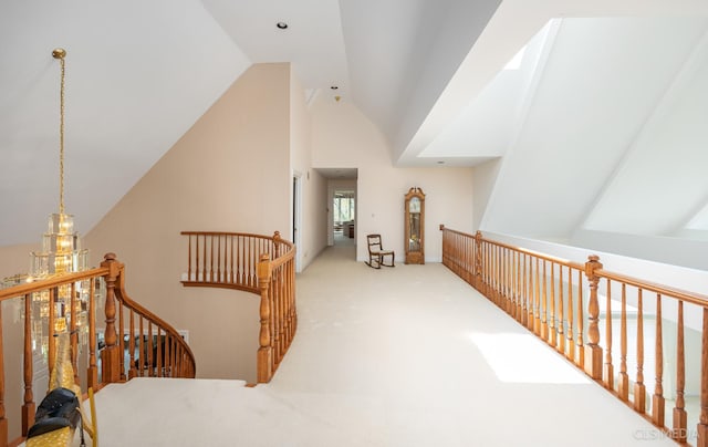 corridor featuring a notable chandelier, vaulted ceiling, and light colored carpet