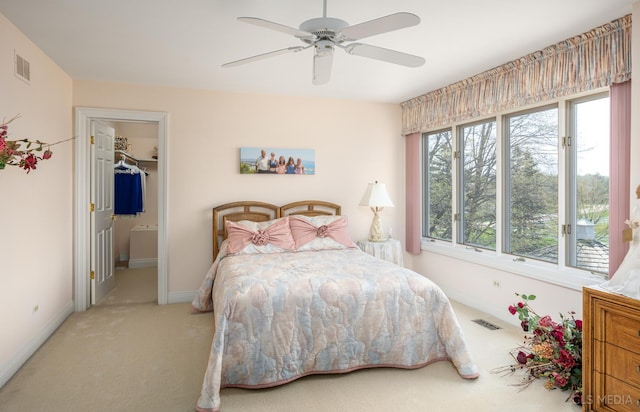 bedroom featuring a closet, a walk in closet, light colored carpet, and ceiling fan