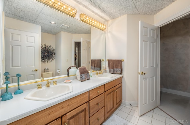 bathroom featuring toilet, dual bowl vanity, tile floors, and a drop ceiling