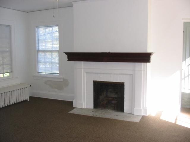 unfurnished living room featuring radiator heating unit and dark colored carpet