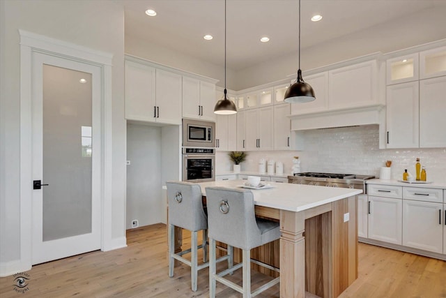 kitchen with a kitchen island, appliances with stainless steel finishes, white cabinetry, hanging light fixtures, and light wood-type flooring