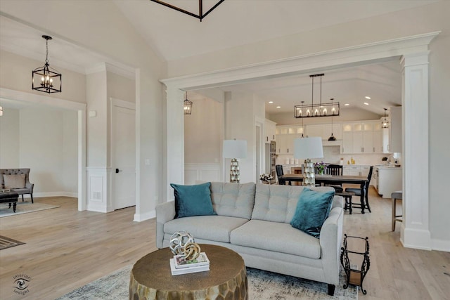 living room with high vaulted ceiling, decorative columns, a notable chandelier, and light wood-type flooring