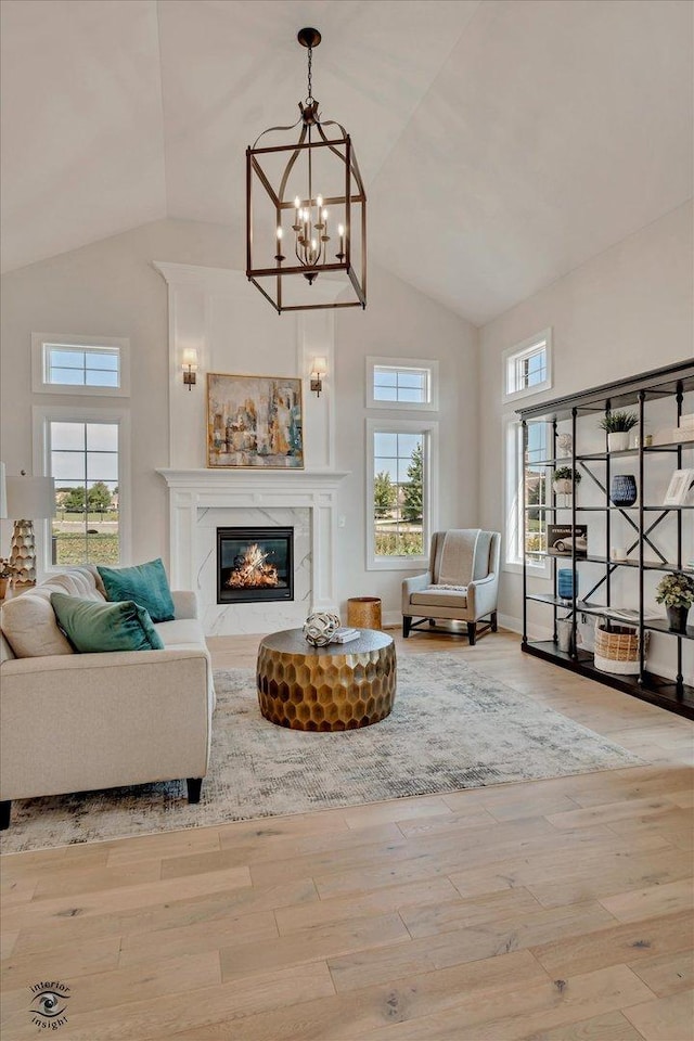 living room with light wood-type flooring, a chandelier, a premium fireplace, and a healthy amount of sunlight