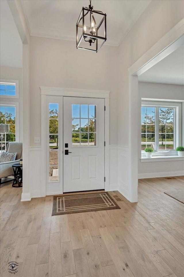 foyer featuring ornamental molding, a notable chandelier, light wood-type flooring, and plenty of natural light