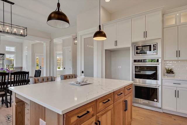 kitchen featuring decorative light fixtures, appliances with stainless steel finishes, light wood-type flooring, white cabinets, and a center island