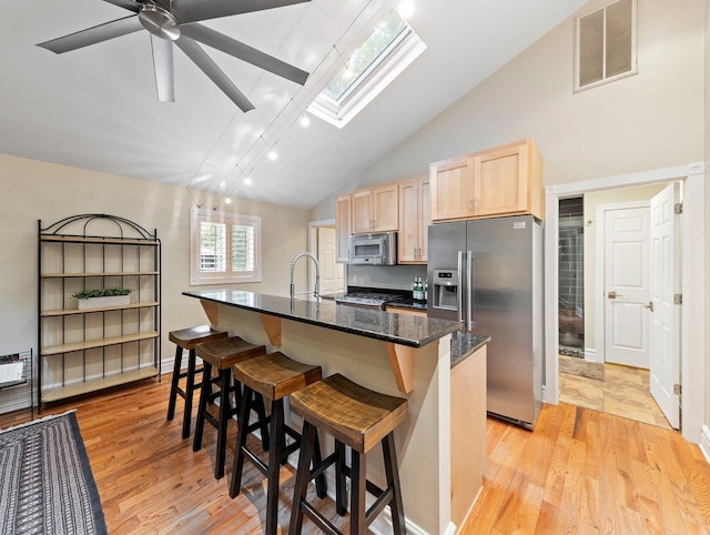 kitchen featuring lofted ceiling with skylight, light brown cabinets, stainless steel appliances, light wood-type flooring, and a kitchen island with sink