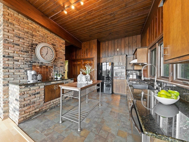 kitchen with appliances with stainless steel finishes, dark stone counters, wood walls, sink, and brick wall