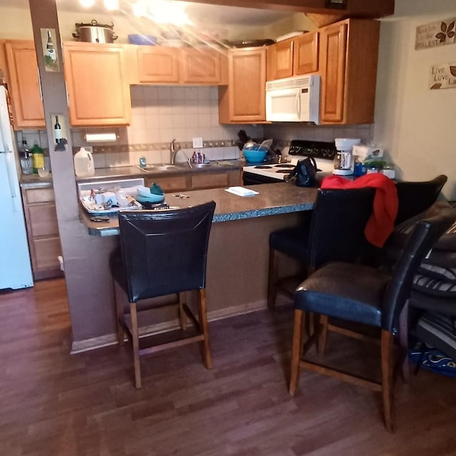 kitchen with kitchen peninsula, white appliances, a kitchen breakfast bar, dark hardwood / wood-style flooring, and tasteful backsplash