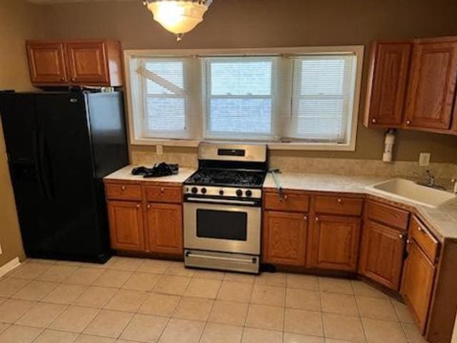 kitchen with sink, stainless steel gas range, black fridge, and light tile floors