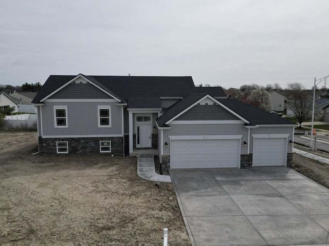 view of front of property featuring stone siding, driveway, an attached garage, and fence