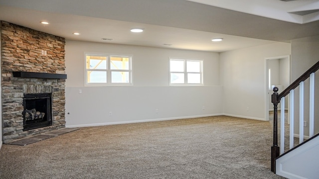 unfurnished living room featuring carpet floors, a stone fireplace, stairway, and baseboards