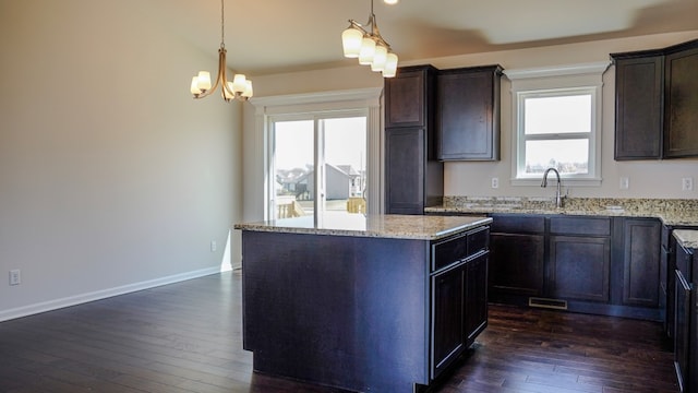 kitchen featuring dark wood-type flooring, a kitchen island, dark brown cabinets, light stone countertops, and baseboards