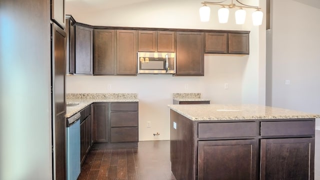 kitchen featuring light stone counters, dark brown cabinetry, stainless steel appliances, dark wood-type flooring, and a center island