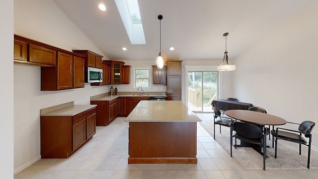 kitchen featuring a skylight, a sink, a kitchen island, hanging light fixtures, and stainless steel microwave