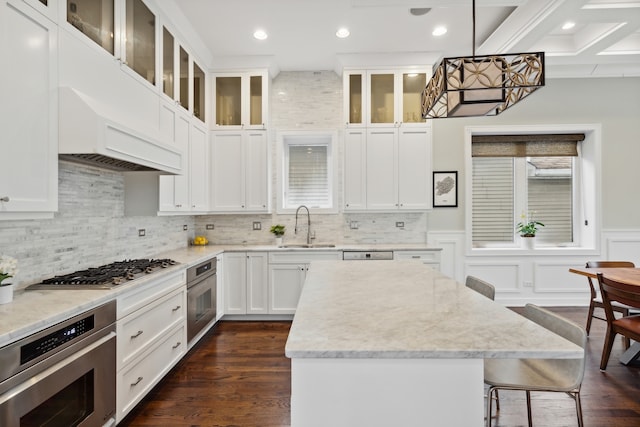 kitchen with a breakfast bar area, white cabinetry, appliances with stainless steel finishes, hanging light fixtures, and dark hardwood / wood-style flooring