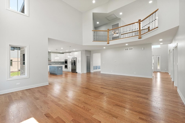 unfurnished living room featuring a high ceiling, recessed lighting, light wood-style floors, and baseboards
