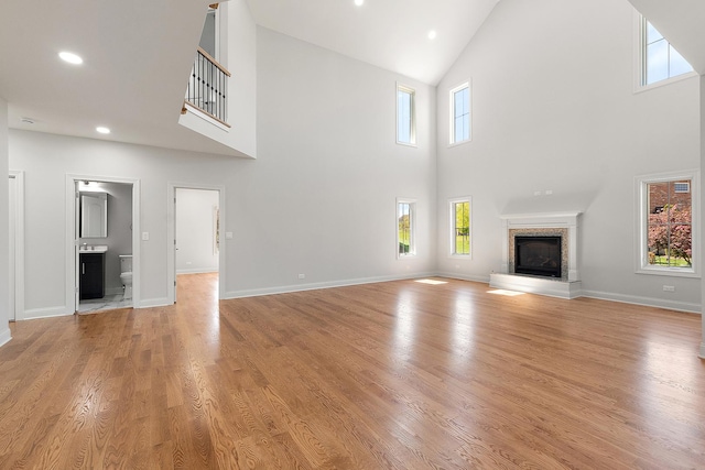 unfurnished living room with high vaulted ceiling, a glass covered fireplace, recessed lighting, light wood finished floors, and baseboards