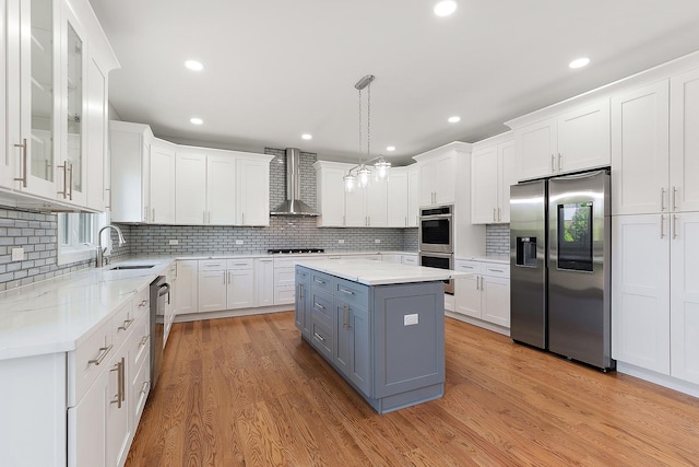 kitchen featuring stainless steel appliances, gray cabinets, wall chimney exhaust hood, a sink, and white cabinetry