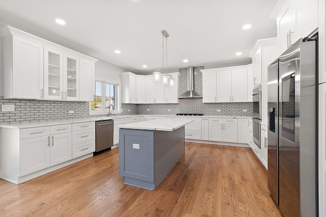 kitchen with wall chimney exhaust hood, stainless steel appliances, white cabinetry, a center island, and decorative backsplash