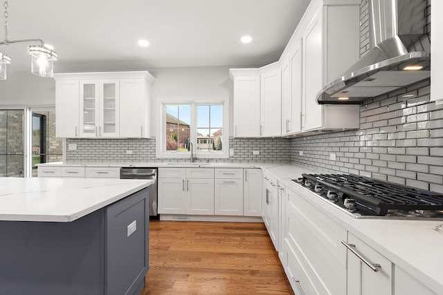 kitchen with appliances with stainless steel finishes, wall chimney range hood, a sink, white cabinetry, and recessed lighting