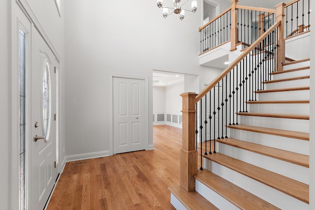 foyer with a towering ceiling, wood finished floors, baseboards, stairway, and a chandelier
