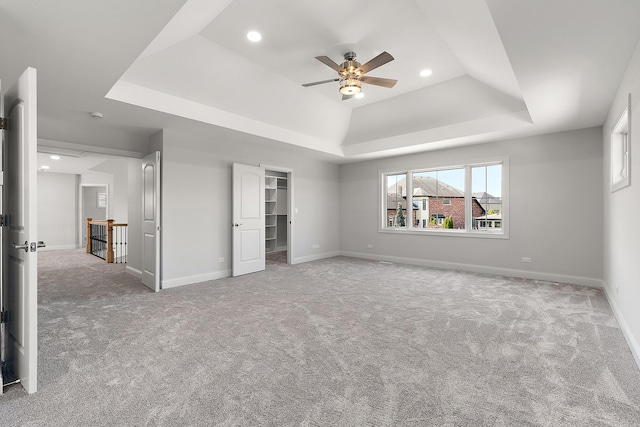 unfurnished bedroom featuring a tray ceiling, carpet, recessed lighting, baseboards, and a walk in closet