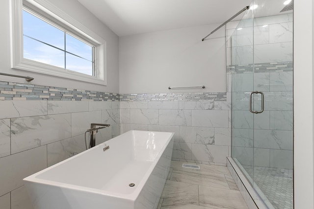 bathroom with marble finish flooring, a shower stall, a freestanding tub, tile walls, and a baseboard radiator