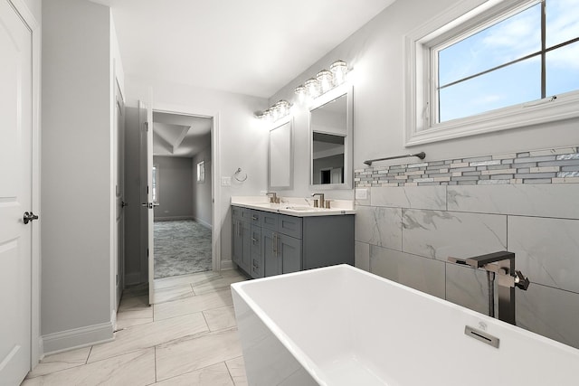 bathroom featuring marble look tile flooring, a freestanding bath, baseboards, and double vanity