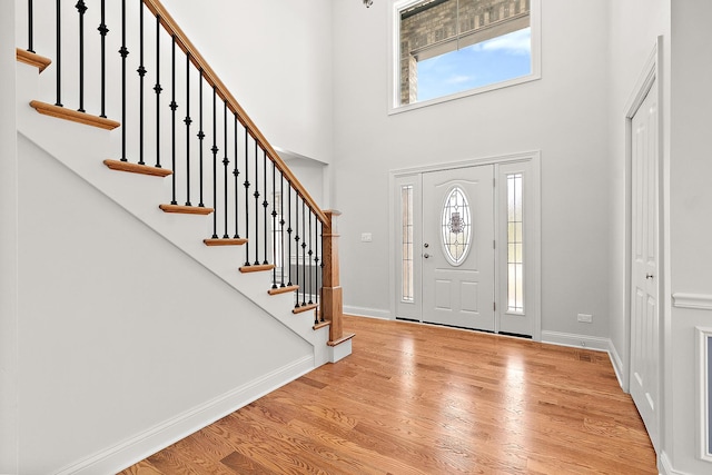 foyer entrance featuring healthy amount of natural light, light wood-type flooring, stairway, baseboards, and a high ceiling