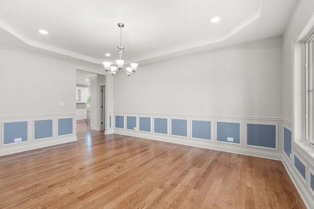 spare room with a raised ceiling, a chandelier, recessed lighting, light wood-style floors, and a decorative wall