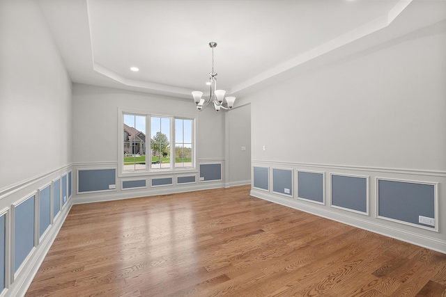 empty room featuring a raised ceiling, a chandelier, wood finished floors, recessed lighting, and a wainscoted wall