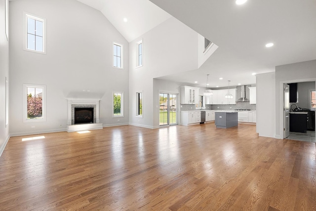 unfurnished living room featuring recessed lighting, light wood-style flooring, a glass covered fireplace, high vaulted ceiling, and baseboards