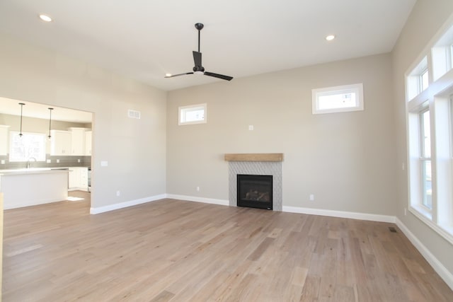 unfurnished living room featuring ceiling fan, a tile fireplace, a healthy amount of sunlight, and light hardwood / wood-style floors