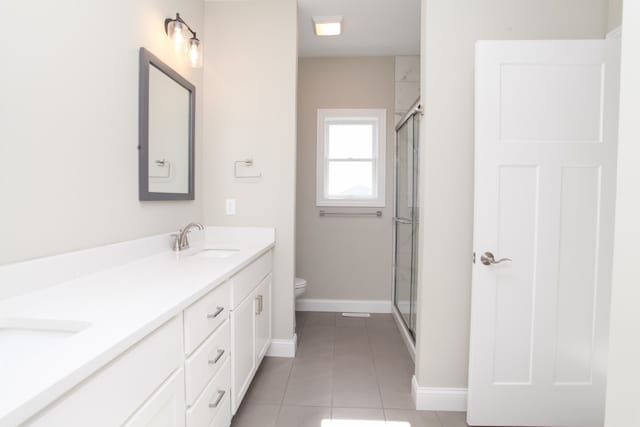 bathroom featuring a shower with door, tile flooring, double vanity, and toilet