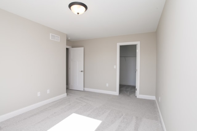 unfurnished bedroom with a closet, light colored carpet, and a walk in closet