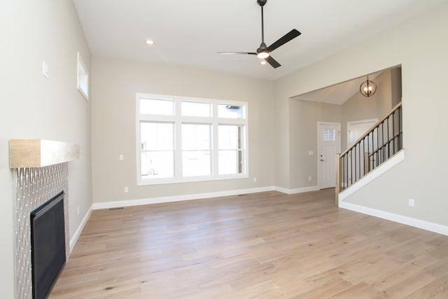 unfurnished living room with a tile fireplace, ceiling fan with notable chandelier, and light hardwood / wood-style floors