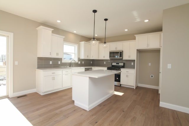 kitchen featuring white cabinetry, stainless steel appliances, light wood-type flooring, a center island, and hanging light fixtures