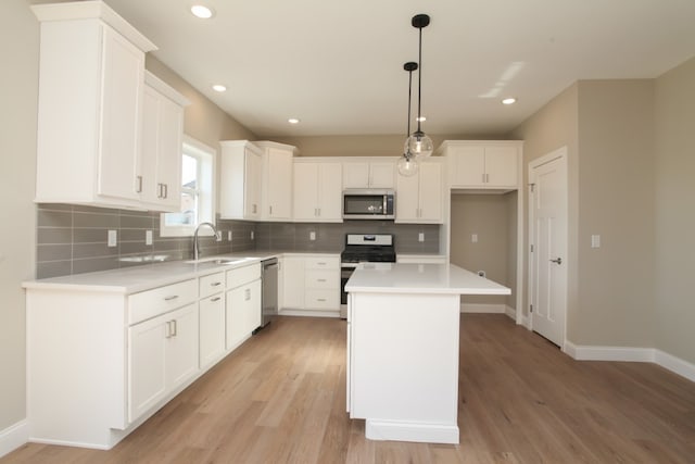 kitchen with white cabinets, appliances with stainless steel finishes, a center island, decorative light fixtures, and light wood-type flooring