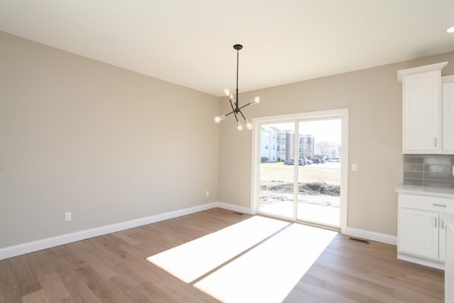 unfurnished dining area with a chandelier and light hardwood / wood-style flooring