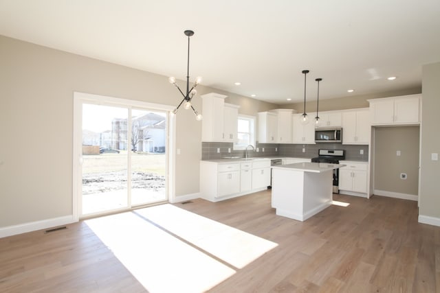 kitchen with hanging light fixtures, an inviting chandelier, appliances with stainless steel finishes, light wood-type flooring, and a center island