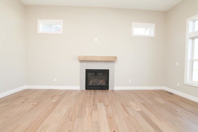 unfurnished living room featuring a tile fireplace, a healthy amount of sunlight, and light hardwood / wood-style floors