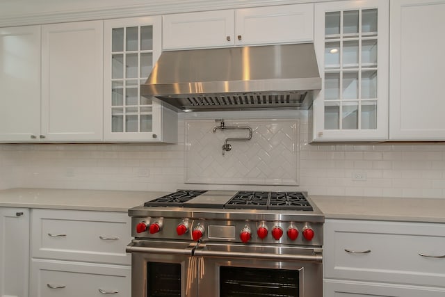 kitchen featuring range hood, white cabinetry, double oven range, and backsplash