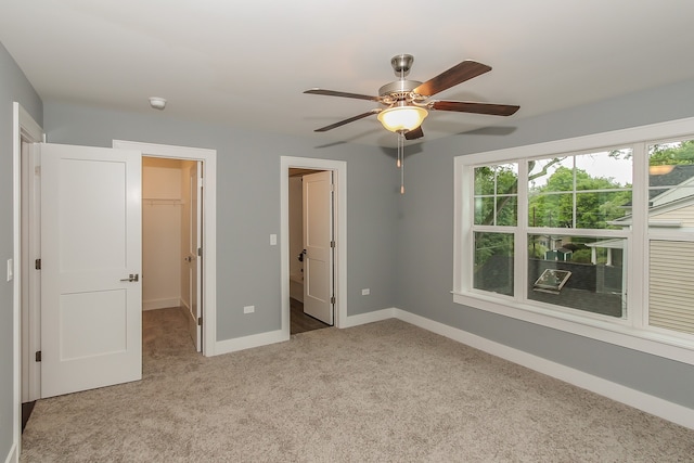 unfurnished bedroom with light colored carpet, a spacious closet, a closet, and ceiling fan